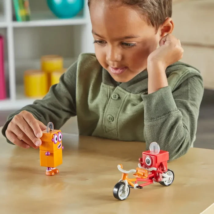 Boy playing with orange Numberblock Two and red Numberblock One figures on a red and orange toy tandem bicycle.
