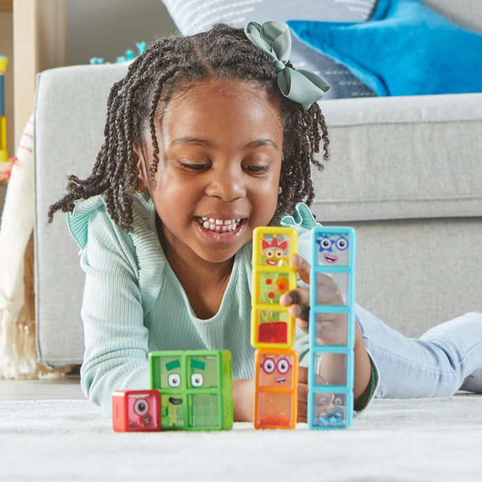 Smiling girl plays with colorful, character-faced transparent blocks of varying heights on a white rug.