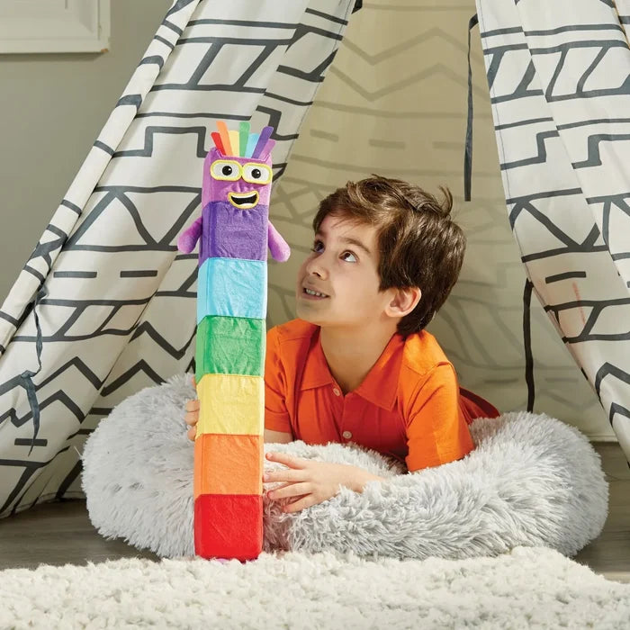 A child looks at a tall plush toy with seven colorful segments and a friendly face inside a patterned play tent.