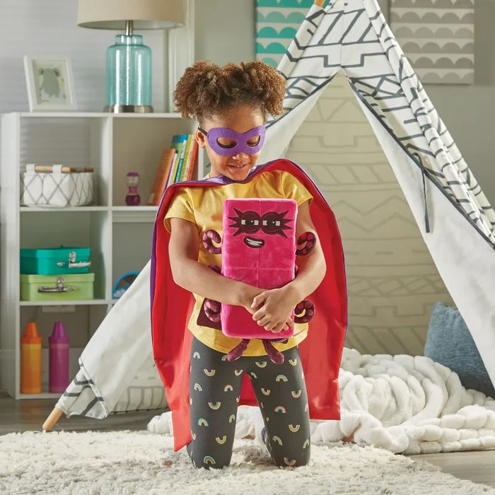 Child in a superhero costume holding a pink rectangular Octoblock plush with eight purple arms in a play tent.