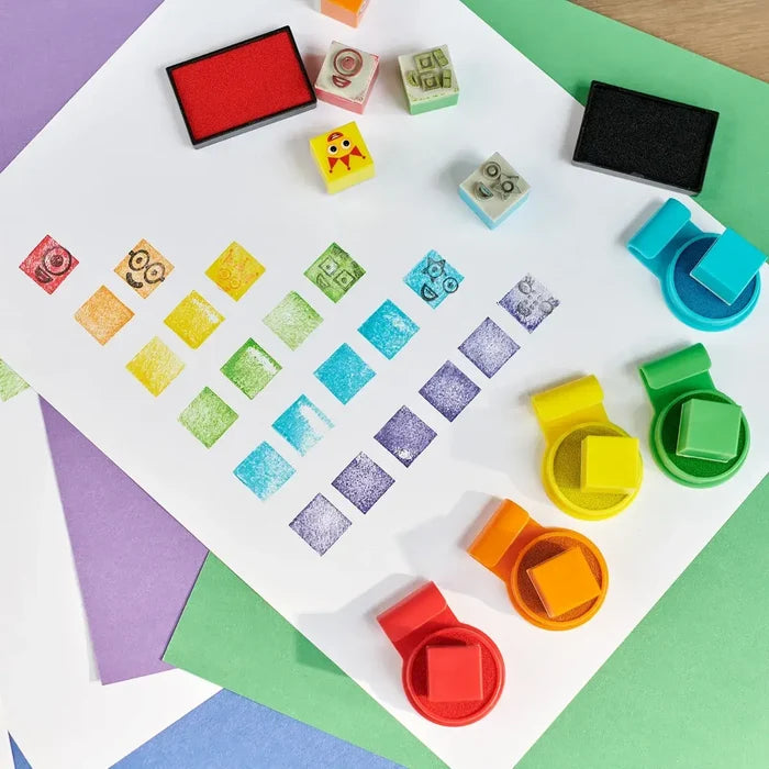 Colorful character face stamps and ink pads with a rainbow grid of stamped squares and faces on white paper.