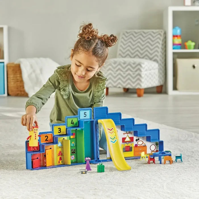 Girl playing with a blue tiered toy featuring numbered doors 1-5, a yellow slide, and colorful miniature figures.
