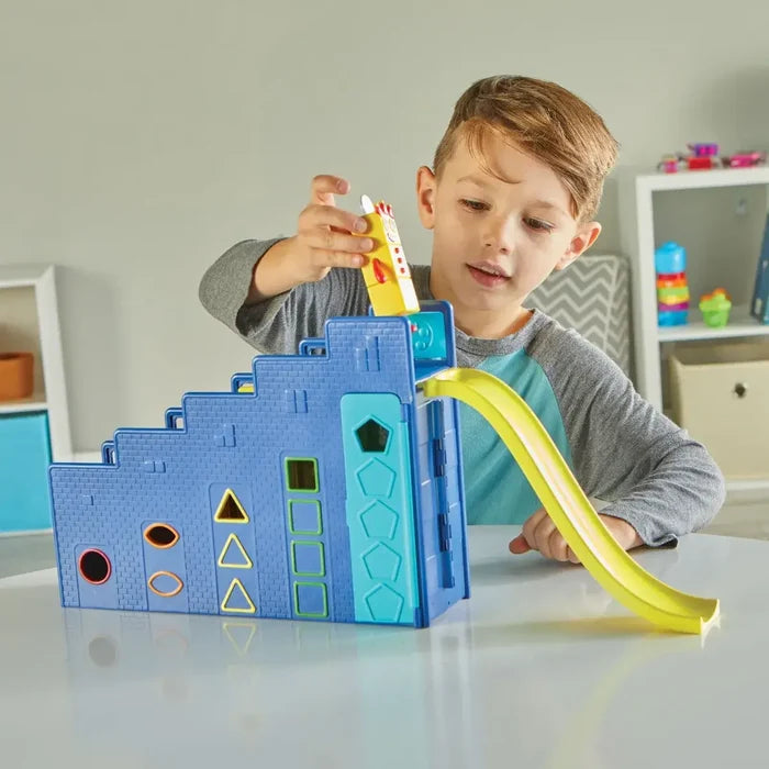 A boy plays with a blue stepped toy building featuring colorful shape cutouts and a curved yellow slide.