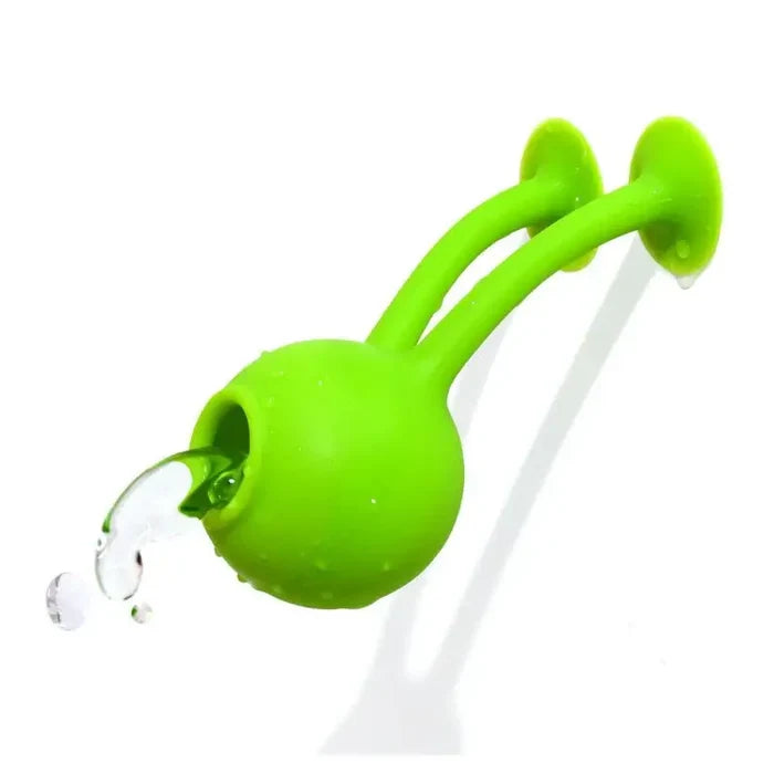 Bright green, ball-shaped silicone toy with two suction cup arms stuck to a wall, holding water in its open mouth.