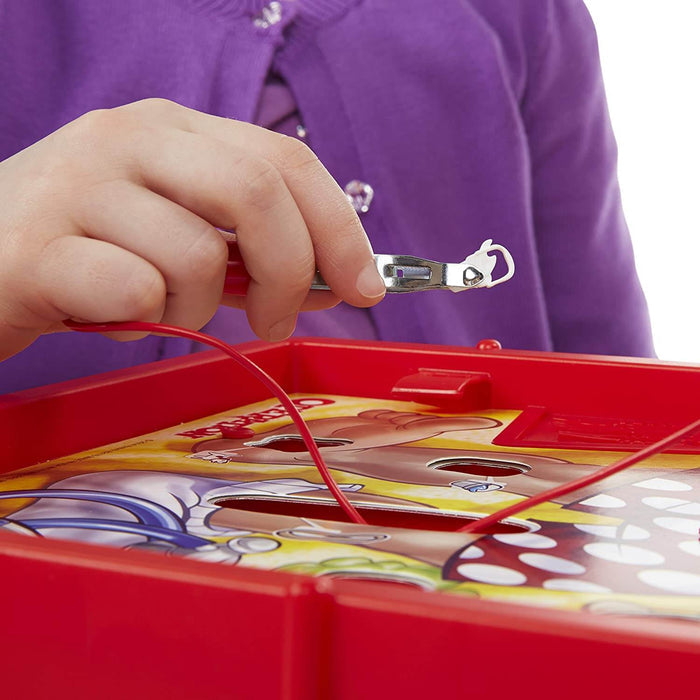 Child's hand using tweezers to pick up a small white piece from a red board game with cartoon character illustrations.