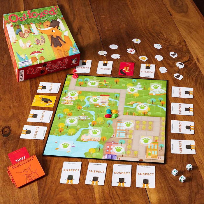 Outfoxed board game with green illustrated box, landscape board, hat pawns, and cards arranged on a wooden table.
