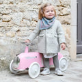 Vintage-style pale pink ride-on car with chrome accents and large white wheels, shown with a young child.
