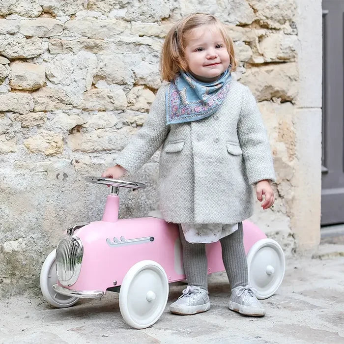 Vintage-style pale pink ride-on car with chrome accents and large white wheels, shown with a young child.