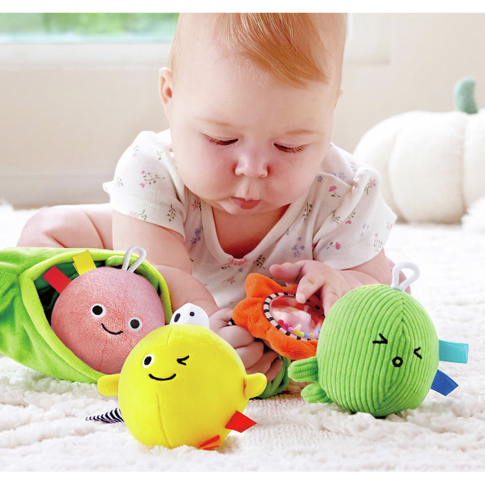 Baby playing with plush toys: a green pod with pink, yellow, and green corduroy characters with friendly faces.