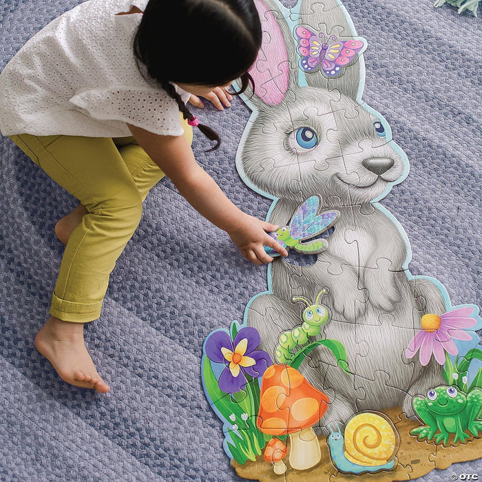 Child assembles a large gray bunny floor puzzle with garden animals and flowers on a blue textured rug.