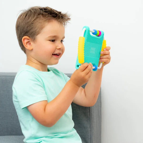 Smiling boy holds a teal and yellow toy mirror featuring textured handles and colorful sliding beads.
