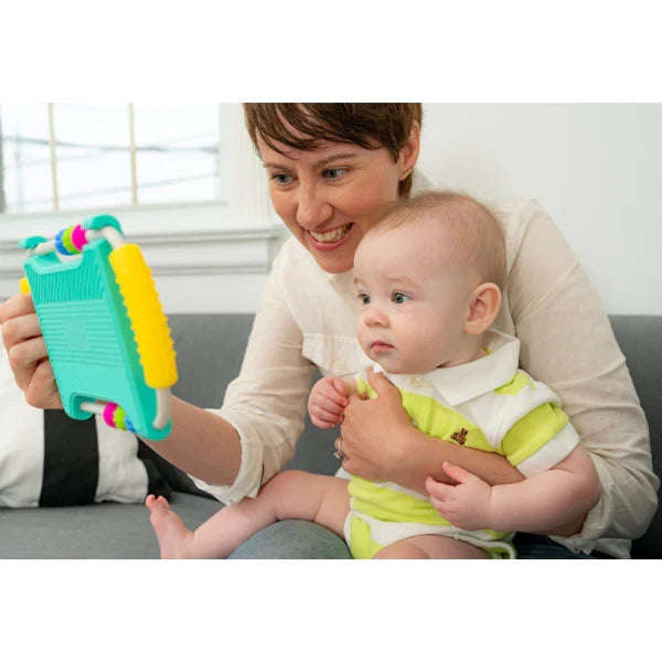 Woman holds a teal and yellow toy mirror with colorful beads for a baby sitting on her lap.