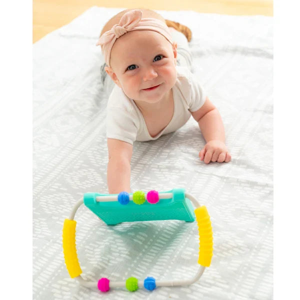 Smiling baby on a patterned mat with a teal mirror toy featuring yellow handles and colorful sliding beads.