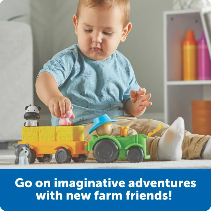 Toddler playing with a green toy tractor pulling a yellow trailer with hay bales and animal figures on a rug.
