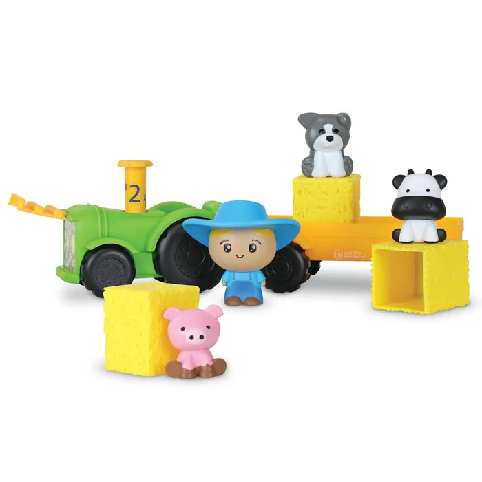 Toy green tractor and trailer with a farmer figure, pig, dog, cow, and three yellow hay bales.
