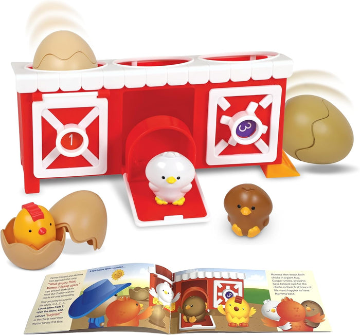 Red toy chicken coop with three colorful chicks, plastic eggs, and an open storybook on a white background.