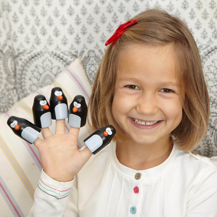 A smiling girl holding up her hand with five black and white penguin game pieces on her fingertips.