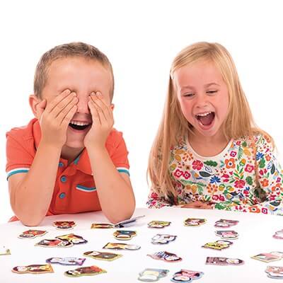 Two children laughing and playing a memory game with colorful penguin-shaped cards on a white table.
