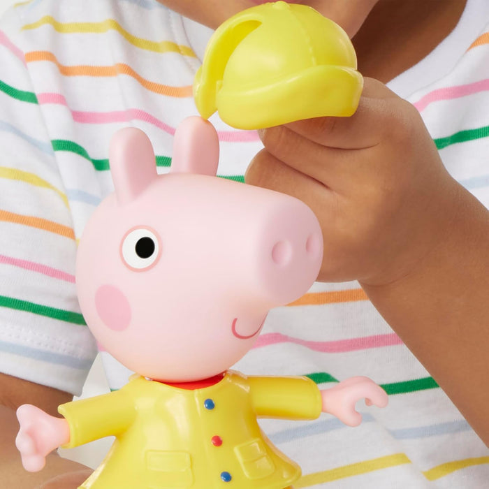 Peppa Pig toy in a yellow raincoat as a child places a matching yellow hat on her head.