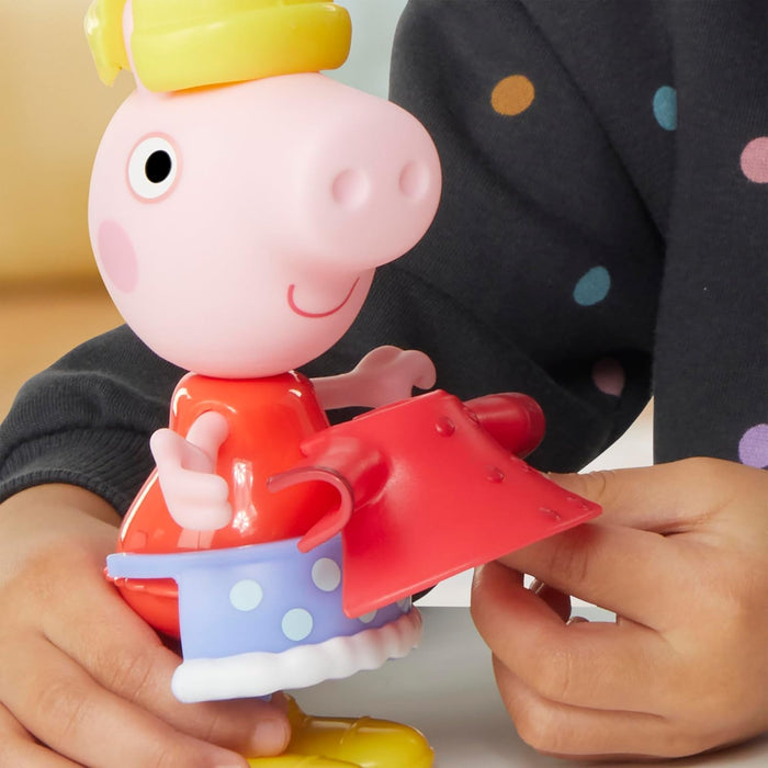 Child's hands snapping a red coat onto a Peppa Pig toy wearing a blue polka-dot skirt and yellow crown.