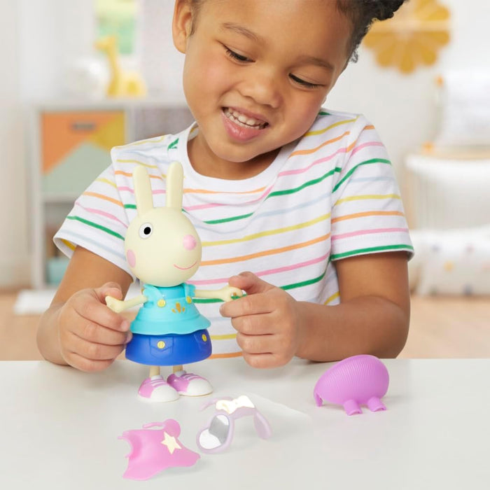 Child playing with a Rebecca Rabbit toy in a blue dress, with pink cape, glasses, and purple hat accessories.