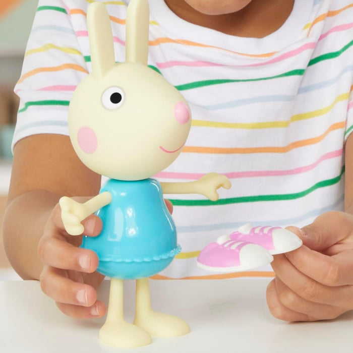 Child holds a cream-colored rabbit toy in a blue dress next to a pair of pink and white slip-on shoes.