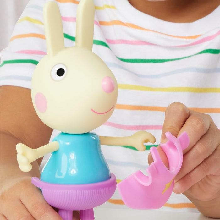 Rebecca Rabbit toy in blue top and purple skirt. A hand holds a pink snap-on clothing accessory.