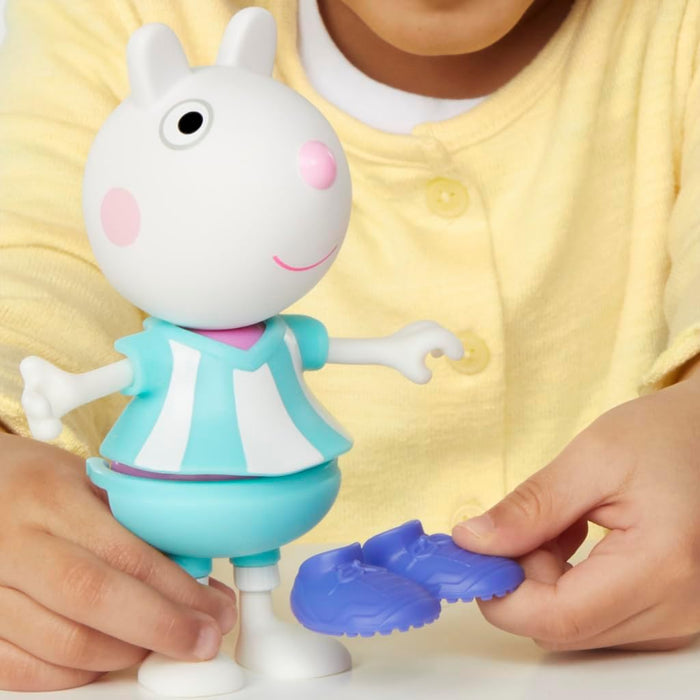 White Suzy Sheep toy in a blue and white striped outfit. A child's hand holds a pair of purple shoes.