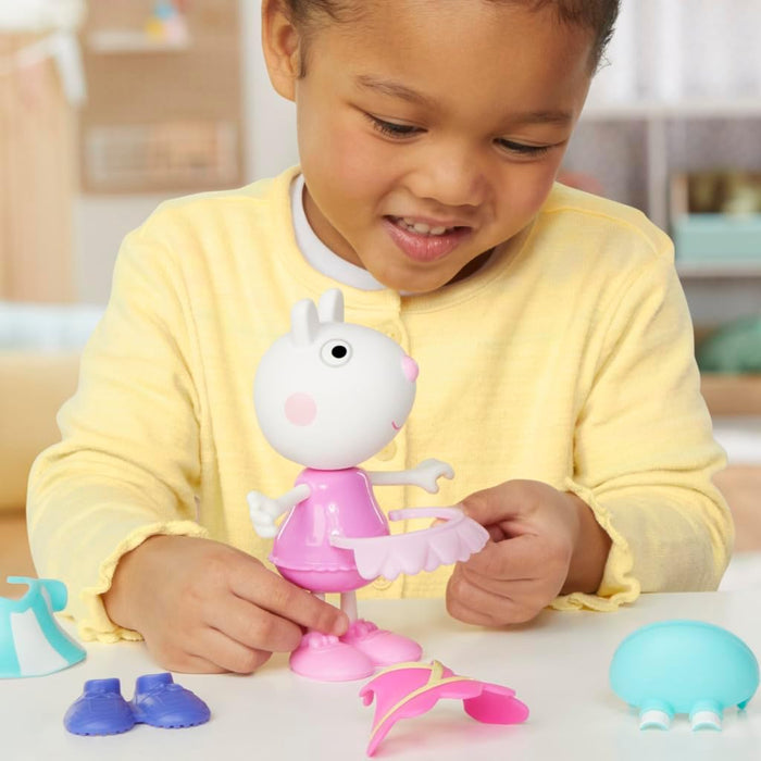 A child dressing a Suzy Sheep toy in a pink tutu, with colorful outfits and shoes laid out on the table.