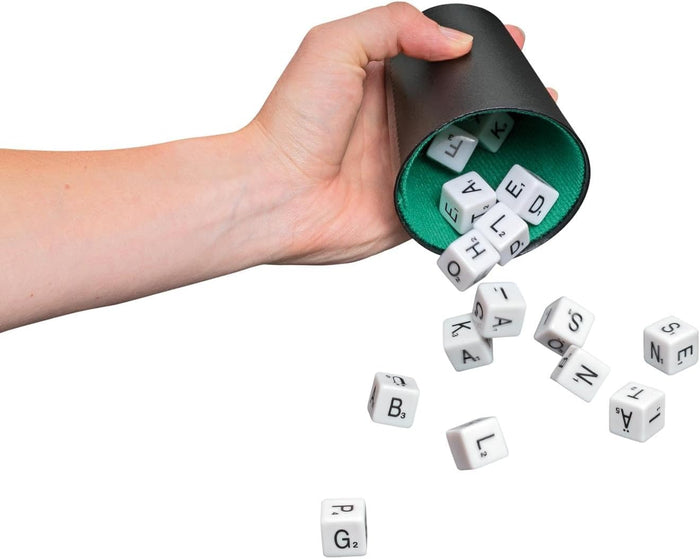 Hand pouring white dice with black letters and point values from a black shaker cup with a green interior.