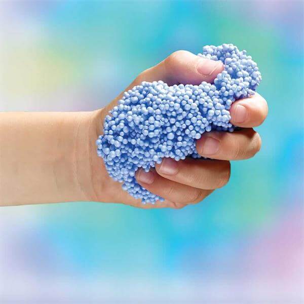 A child's hand squeezing a textured clump of light blue foam beads.