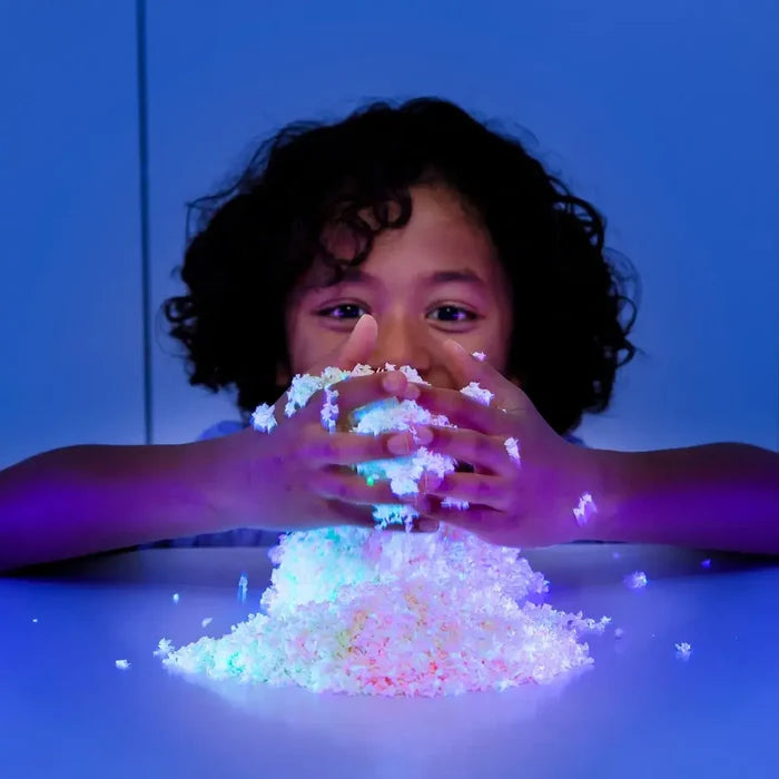 Child holding a glowing pile of white and neon foam bits that sparkle under blue light.