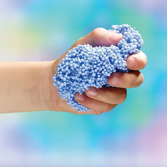A child's hand squeezing a clump of small blue foam beads against a colorful, blurred background.