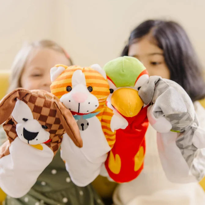 Two girls holding four plush animal hand puppets: a checkered dog, striped cat, red parrot, and grey rabbit.