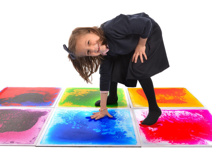 A child plays on six colorful square liquid-filled sensory floor tiles, showing how the fluid moves under pressure.
