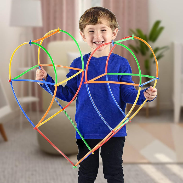 A smiling boy holds a large heart-shaped structure built from colorful, flexible straws and plastic connectors.