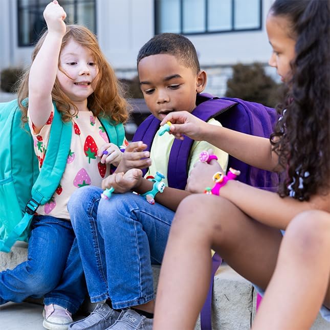Three children wear and share colorful silicone charms in animal and character shapes as rings and bracelets outdoors.