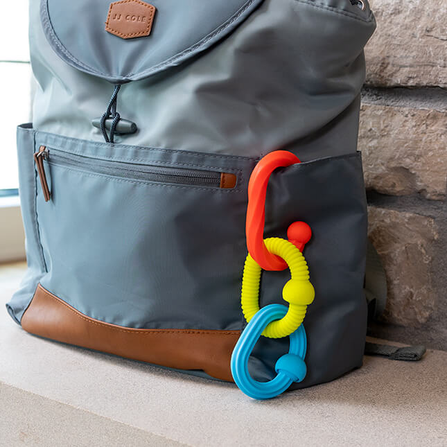 Three textured interlocking links in orange, yellow, and blue hanging from the side pocket of a gray backpack.