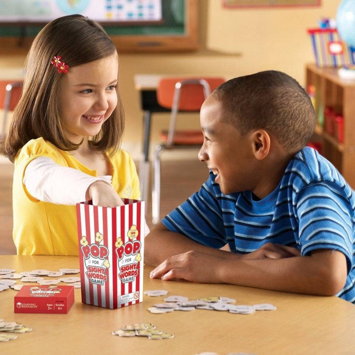 Two children play an educational game with popcorn-shaped word cards and a red and white striped popcorn box.