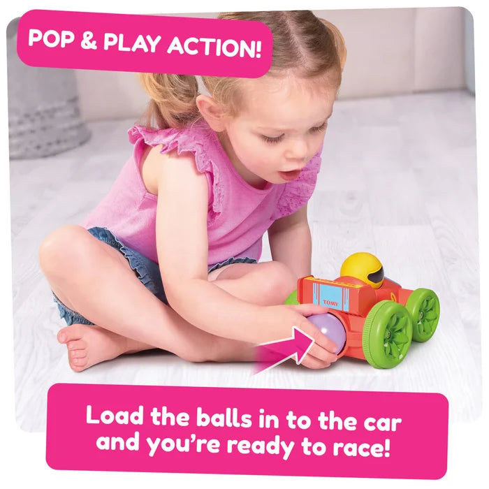 Young girl inserting a purple ball into a red toy car with large green wheels and a yellow driver.