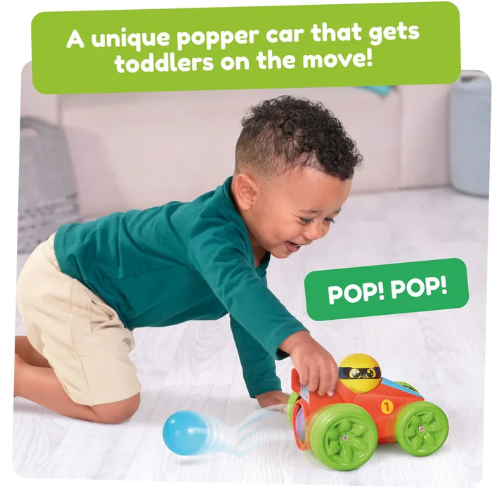 Toddler pushes a red race car with green wheels that pops out a blue ball as it rolls on the floor.