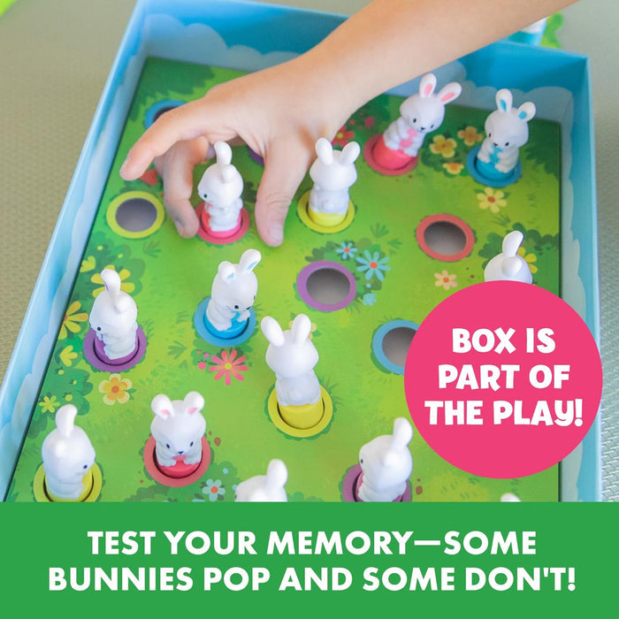 Child playing a memory game by pressing white bunny figures into colorful holes on a grassy field board inside a box.
