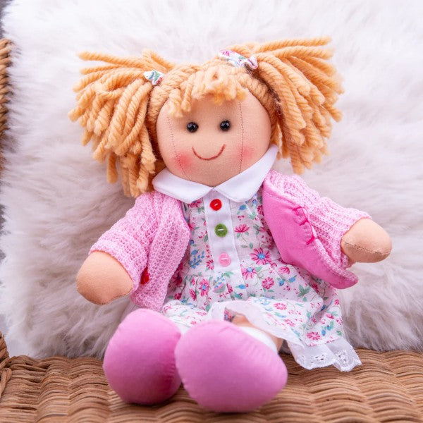 Blonde rag doll with yarn pigtails, pink cardigan, and floral dress with colorful buttons on white faux fur.