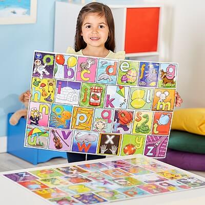 Young girl holding a colorful alphabet board with letter illustrations; another board sits on the table.