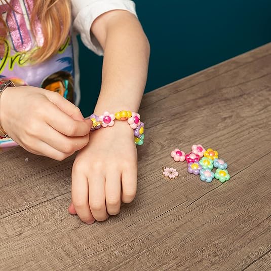 Child's hands popping colorful flower-shaped beads onto a bracelet, with more beads scattered on a wooden table.