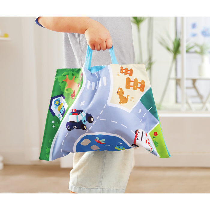 Child holding a blue fabric bag featuring a colorful road map illustration with a police car, pond, and orange cat.