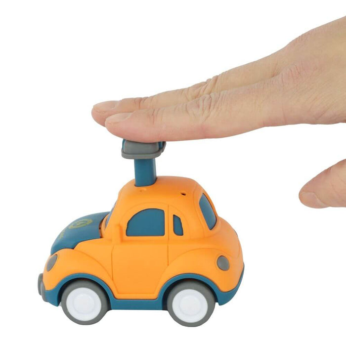 Hand pressing down on the blue plunger of a rounded orange toy car with blue trim and white wheels.
