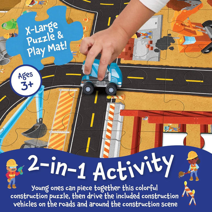 Hand moving a blue toy truck on a colorful construction puzzle mat featuring roads and work site illustrations.