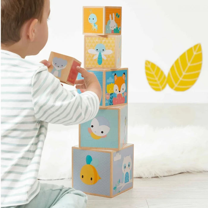 Toddler stacking six wooden blocks with cute pastel animal illustrations like a fox, owl, and fish.