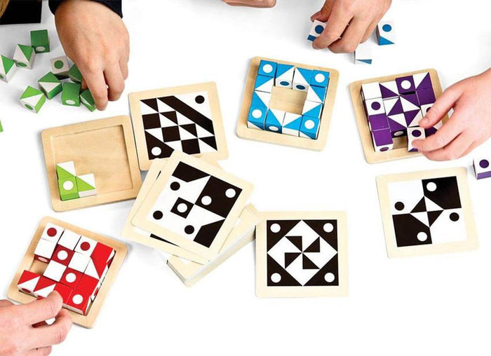Hands arranging colorful patterned cubes in wooden trays to match black and white geometric design cards.